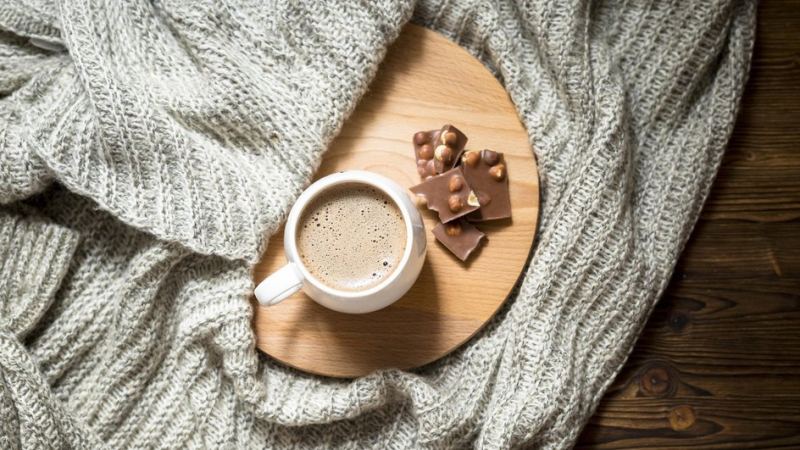 Чашка кофе с шоколадкой и пледом на кровати 