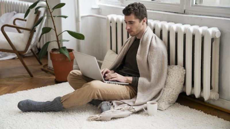 мужчина в пледе сидит у батареи с ноутбуком на коленях