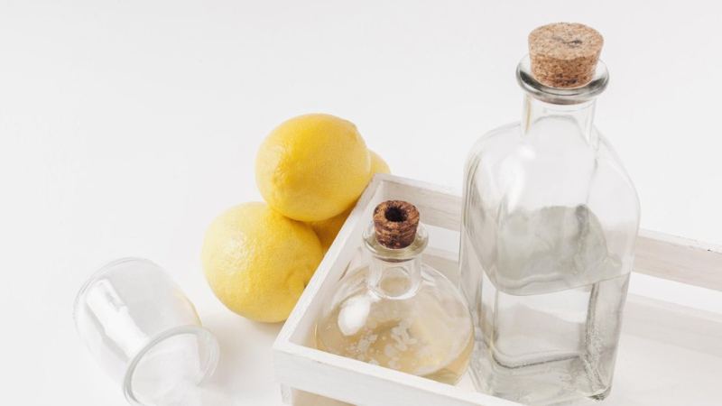 Бутылочки с уксусом, которые помогают в очистке от загрязнений, стоят в белой коробке рядом с лимонами и содой
