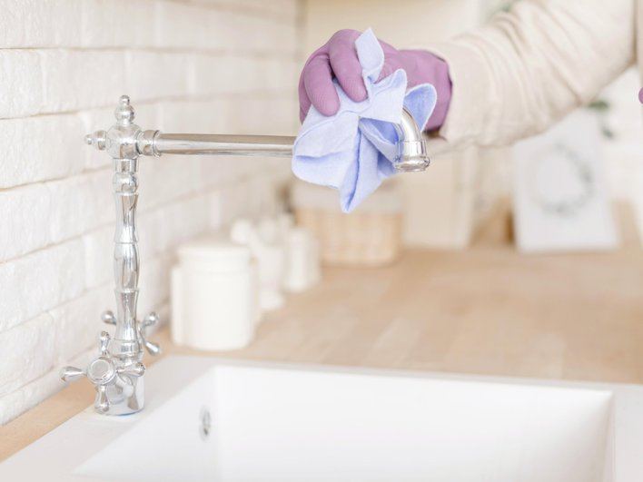 Женщина отмывает жирный налет на кране и раковине 